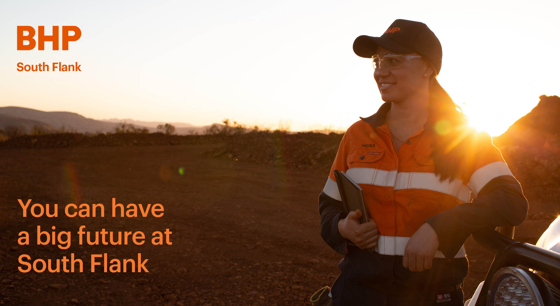 Key image showing a women wearing BHP branded hi-vis gear on a mine site at sunrise.