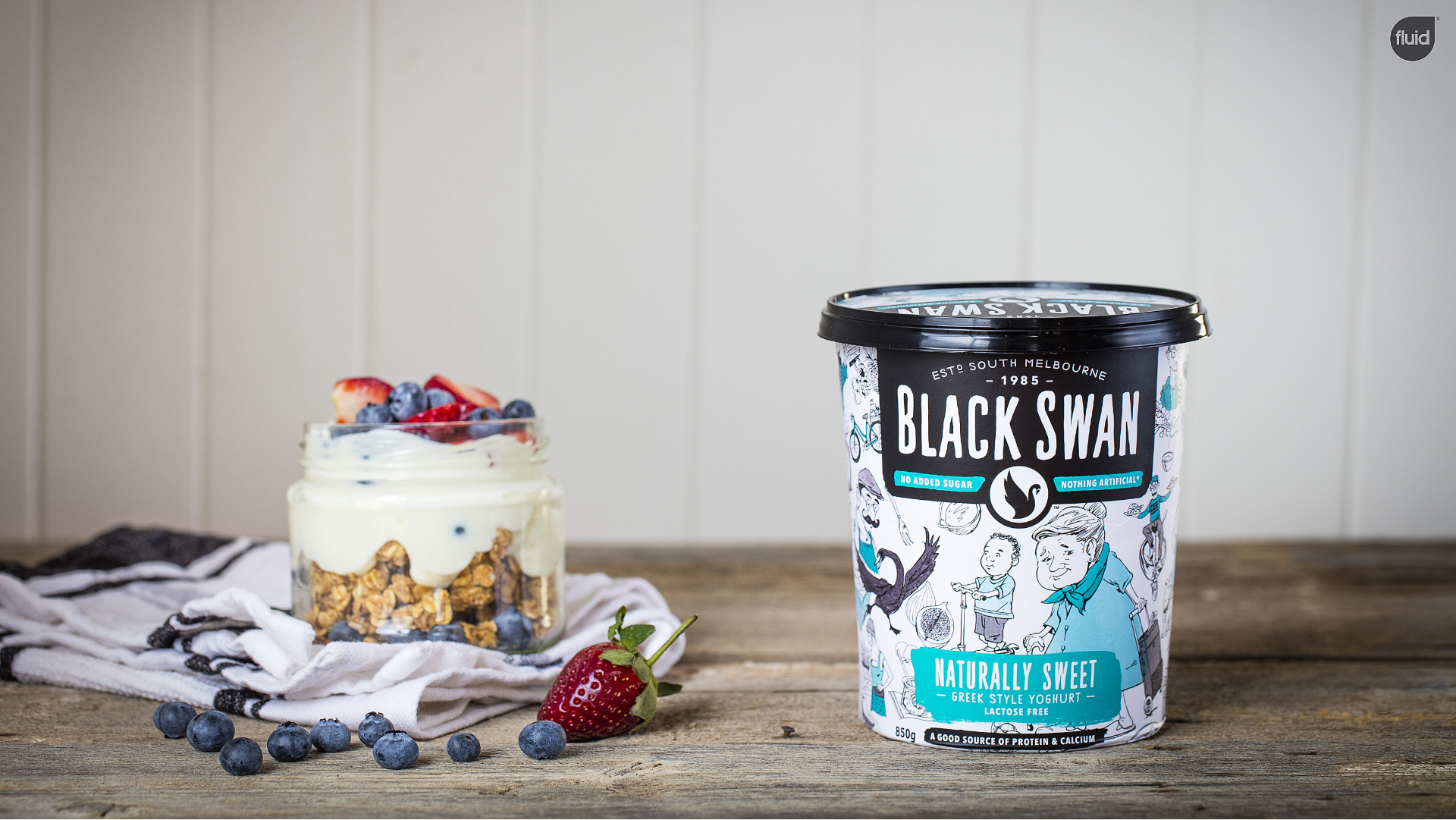 Black Swan Lactose Free Naturally Sweet Greek Style Yoghurt packaging, placed next to granola, yoghurt and berries.