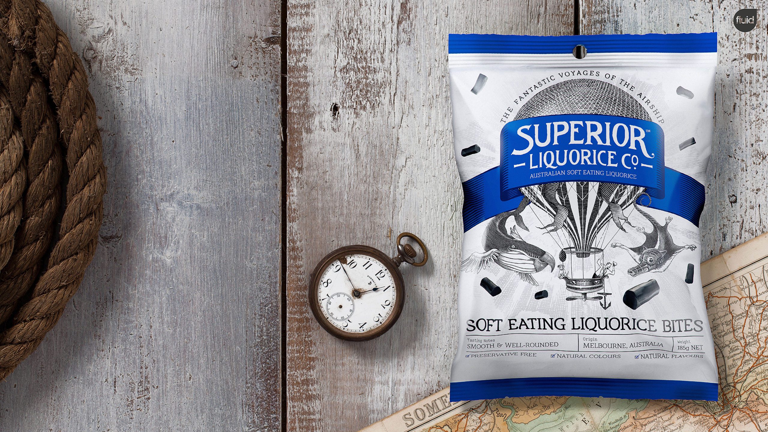 Superior Liquorice Co soft eating liquorice bites product packaging, resting on a wooden surface next to vintage pocket watch and map.