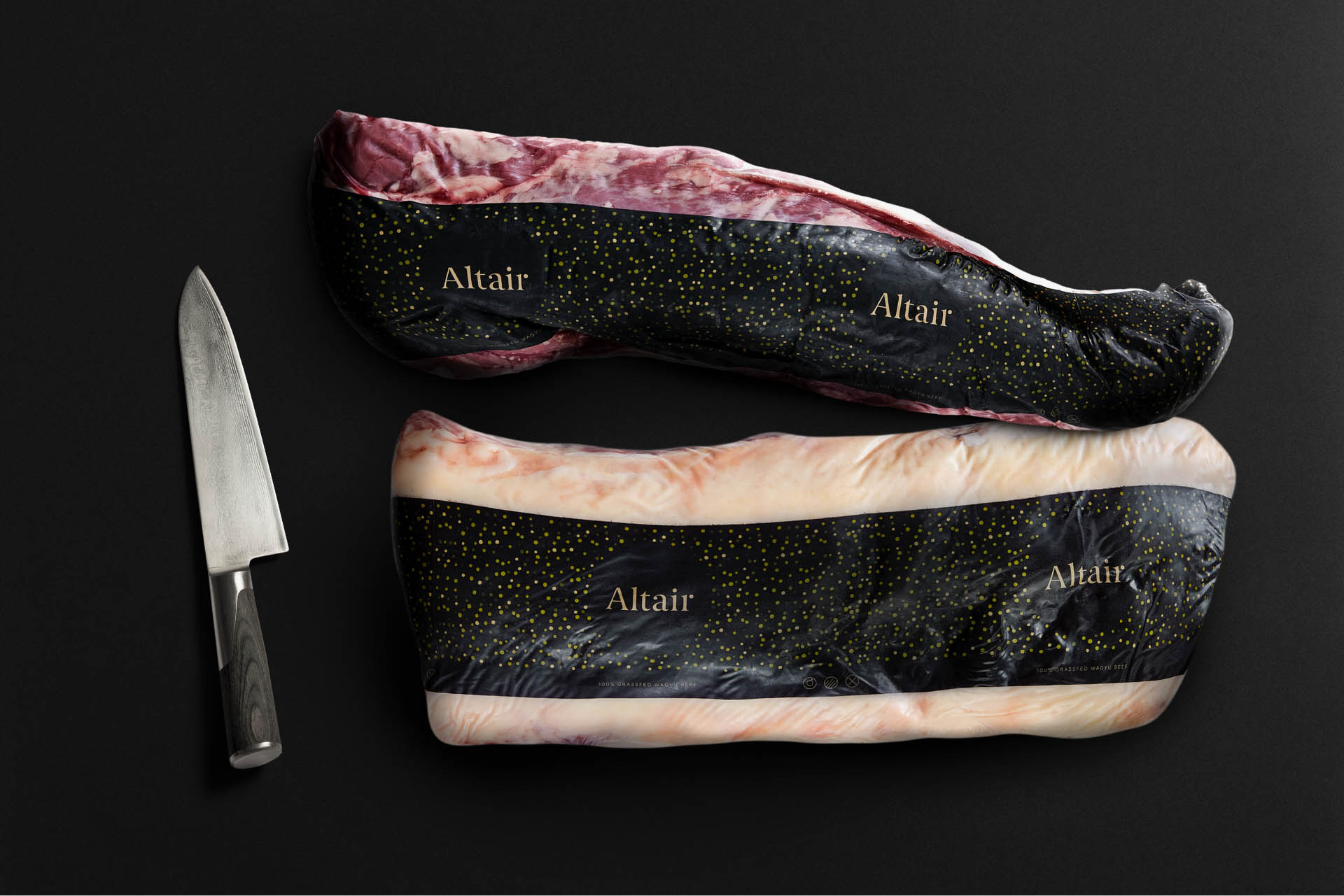 Two shrink wrapped piece's of meat, with Altair branding on them, next to a meat cutting knife.