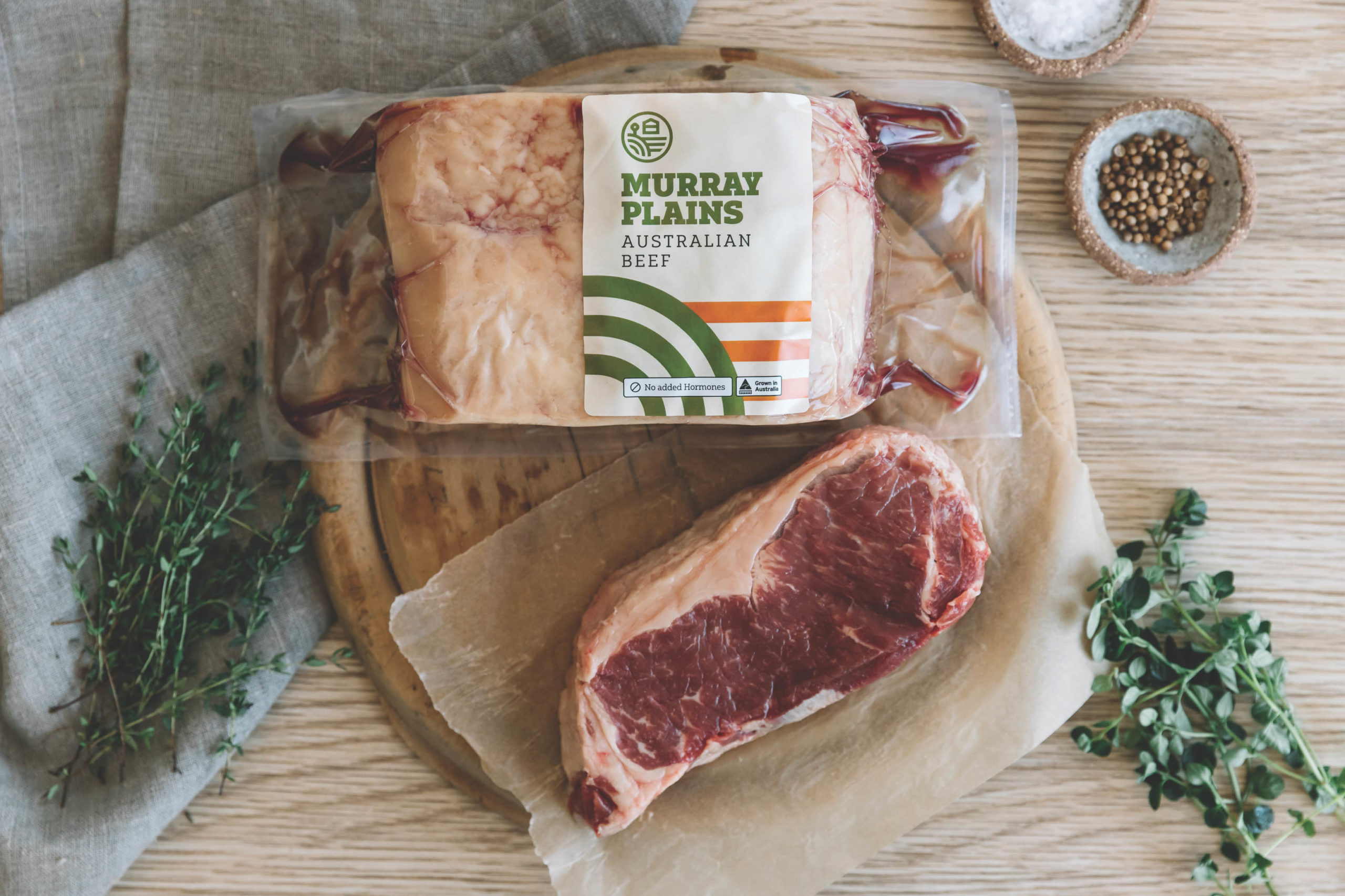 Murray Plains Australian Beef Shrink Wrap packaging, resting on a wooden table, with various ingredients surrounding the raw meat.