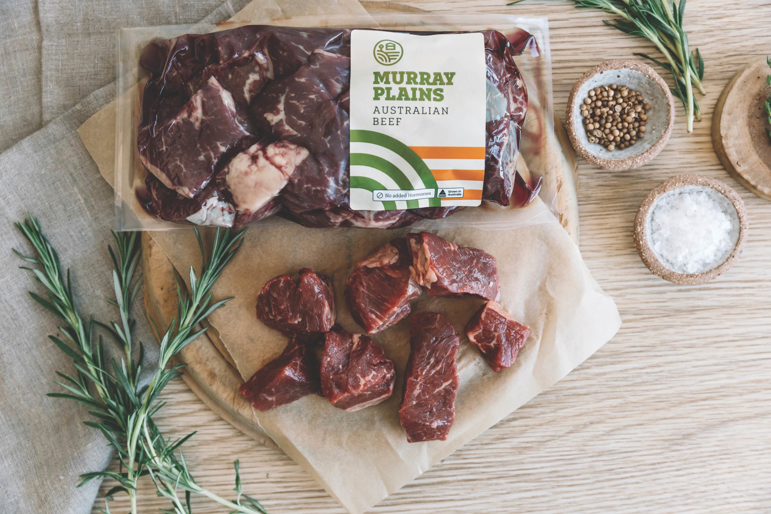 Murray Plains Australian Beef Shrink Wrap packaging, resting on a wooden table, with various ingredients surrounding the raw meat.