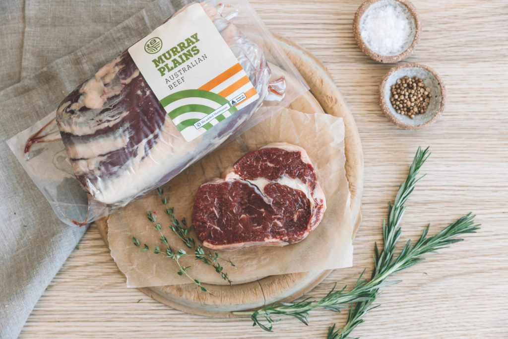 Murray Plains Australia Beef shrink-wrap packaging, next to an uncooked steak wit rosemary and thyme herbs.