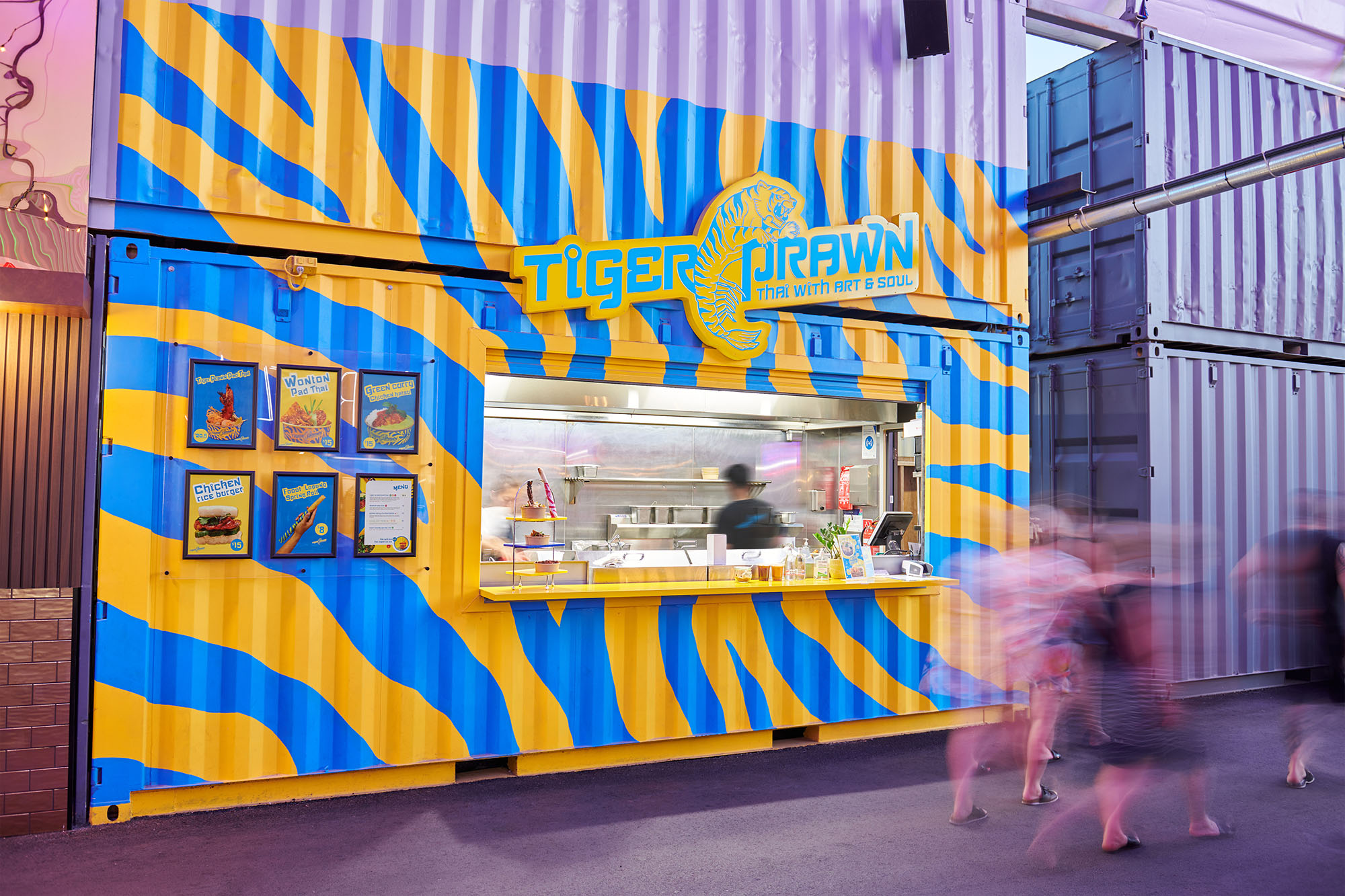 Blue and yellow tiger printed shipping container food truck with people walking by